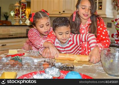 Children in kitchen wearing pyjamas rolling out dough with rolling pin