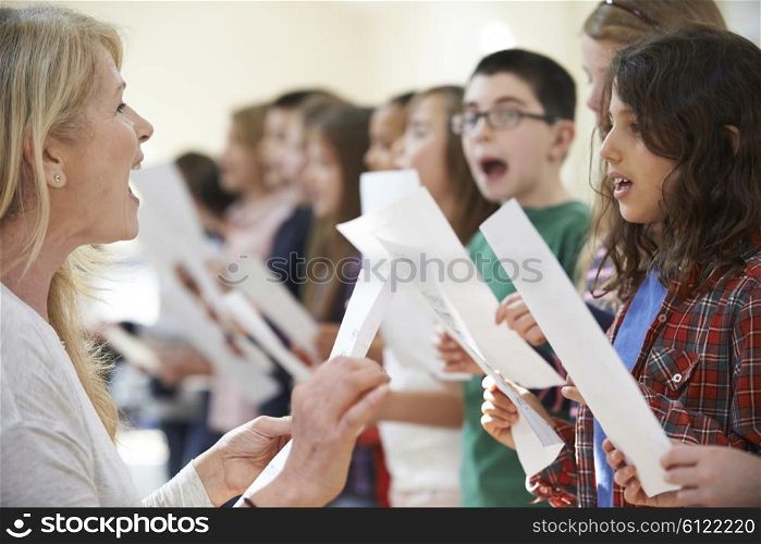 Children In Singing Group Being Encouraged By Teacher
