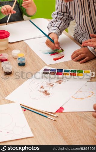 Children learn to paint with a brush and watercolors on paper in the kindergarten. Children are painting