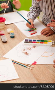 Children learn to paint with a brush and watercolors on paper in the kindergarten. Children are painting