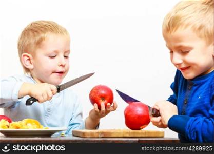 Children little boys brothers playing dangerous game with kitchen knife cutting apple, making salad at home.