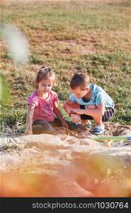 Children, little girls and boy, playing in sandbox in playground outside on summer day. Real people, authentic situations