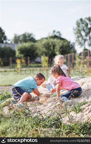 Children, little girls and boy, playing in sandbox in playground outside on summer day. Real people, authentic situations