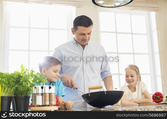 Children looking at father preparing food in kitchen