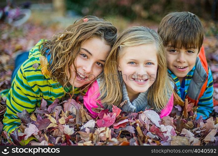 Children lying on autumn leaves in garden