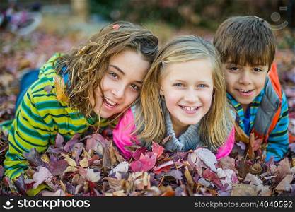 Children lying on autumn leaves in garden