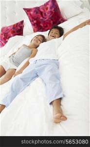 Children Lying On Bed In Pajamas Together