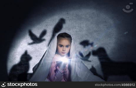 Children nightmare. Cute girl in bed under blanket with flash light