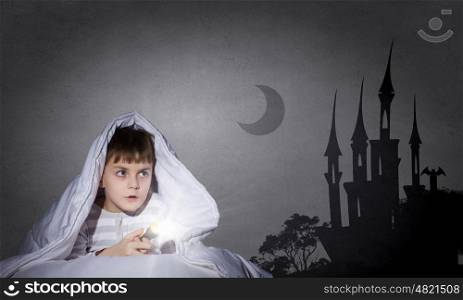 Children nightmare. Little cute boy sitting in bed under blanket with flashlight