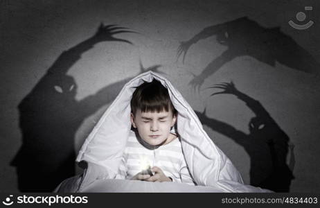 Children nightmare. Little cute boy sitting in bed under blanket with flashlight