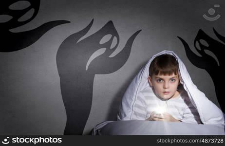 Children nightmare. Little cute boy sitting in bed under blanket with flashlight