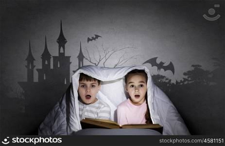 Children nightmares. Two little kids reading book under blanket
