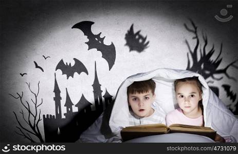 Children nightmares. Two little kids reading book under blanket