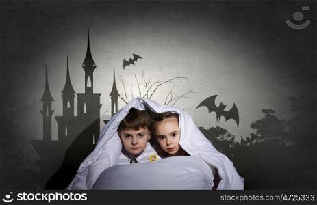 Children nightmares. Two little kids with flashlight under blanket