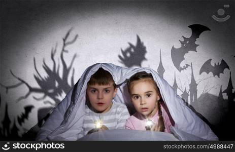 Children nightmares. Two little kids with flashlight under blanket