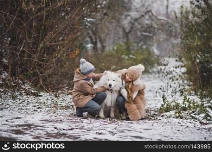Children on a snowy path playing with the white dog.. A boy and a girl gently petting your beloved Samoyed 9844.