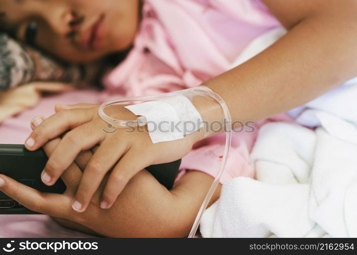 children patient lying on bed of hospital with playing mobile phone and receiving saline.