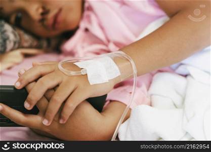 children patient lying on bed of hospital with playing mobile phone and receiving saline.
