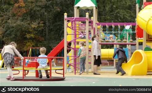 Children playing in an outdoor playground clambering over the brightly coloured equipment in the sunshine having fun