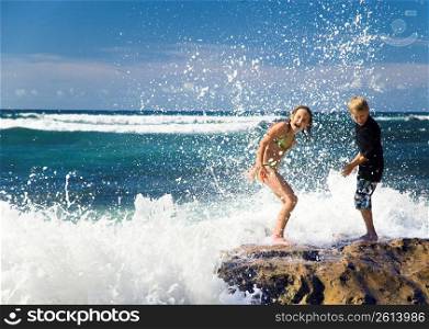 Children playing in ocean on rocks