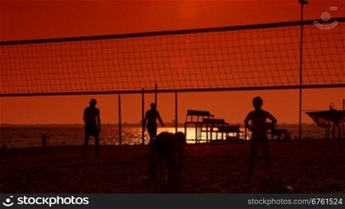 Children playing volleyball on the beach at sunset
