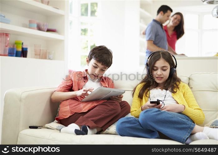 Children Playing With Digital Devices As Parents Make Meal