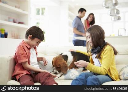 Children Playing With Dog On Sofa As Parents Make Meal