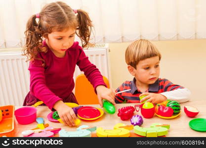 Children playing with housewares and artificial fruit in kindergarten. Children playing cooks