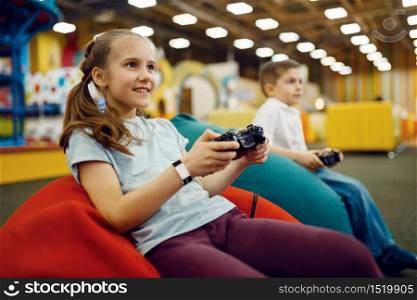 Children plays a game console in the entertainment center. Girl and boy leisures on holidays, childhood happiness, happy kids. Children plays game console, entertainment center
