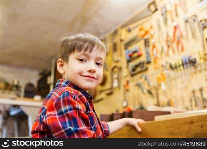 children, profession, carpentry, woodwork and people concept - happy little boy with wood plank at workshop