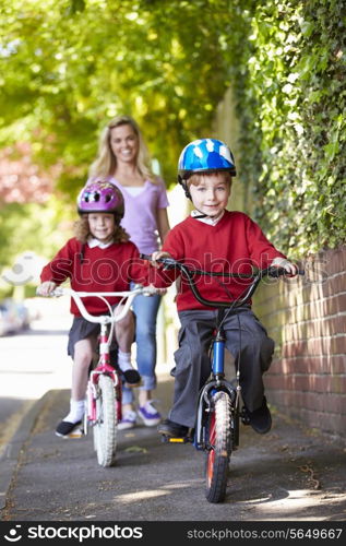 Children Riding Bikes On Their Way To School With Mother