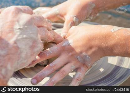 Children&rsquo;s and adult hands work with clay on a potter&rsquo;s wheel. Potter teaches a child to create a product from clay.. Children&rsquo;s and adult hands work with clay on a potter&rsquo;s wheel