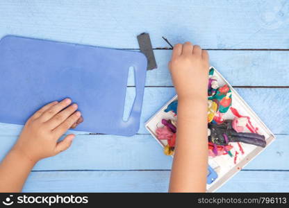 children's hands sculpt figures of clay on a blue table. the view from the top