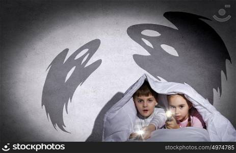 Children&rsquo;s nightmares. Children sitting in bed under blanket with flashlights