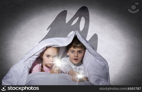 Children&rsquo;s nightmares. Children sitting in bed under blanket with flashlights