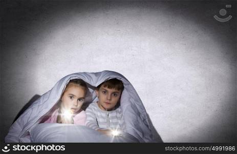 Children&rsquo;s nightmares. Children sitting in bed under blanket with flashlights