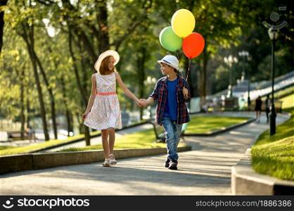 Children&rsquo;s romantic date in summer park, friendship, first love. Boy and girl walking with air balloons. Kids having fun outdoors, happy childhood. Boy and girl walking with air balloons in park