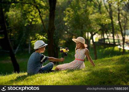 Children&rsquo;s romantic date in summer park, friendship, first love. Boy gives bouquet to a girl. Kids having fun outdoors, happy childhood. Children&rsquo;s date, boy gives bouquet to a girl