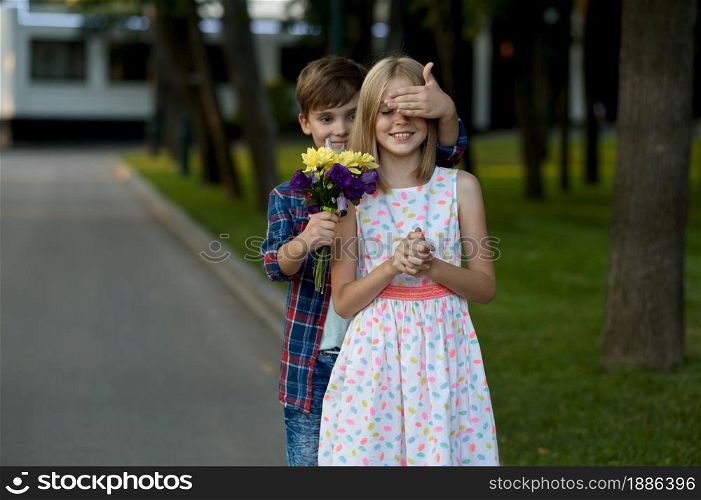 Children&rsquo;s romantic date in summer park, friendship, first love. Boy with bouquet makes surprise to a girl. Kids having fun outdoors, happy childhood. Children&rsquo;s date, boy makes surprise to a girl