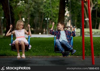Children&rsquo;s romantic date in summer park, friendship, first love. Boy and girl on swings. Kids having fun outdoors, happy childhood. Children&rsquo;s romantic date, boy and girl on swings