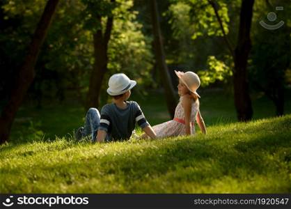 Children&rsquo;s romantic date in summer park, friendship, first love. Boy and girl with air balloons sitting on a grass. Kids having fun outdoors, happy childhood. Boy and girl with air balloons sitting on a grass