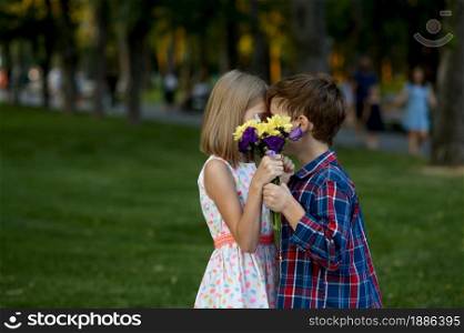Children&rsquo;s romantic date in summer park, friendship, first love kiss. Boy and girl with bouquet on walk path. Kids having fun outdoors, happy childhood. Children&rsquo;s romantic date, first love kiss