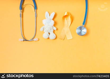 Children&rsquo;s toy rabbit with a Childhood Cancer Awareness yellow ribbon and stethoscope on yellow background with copy space, top view. Childhood Cancer Awareness concept