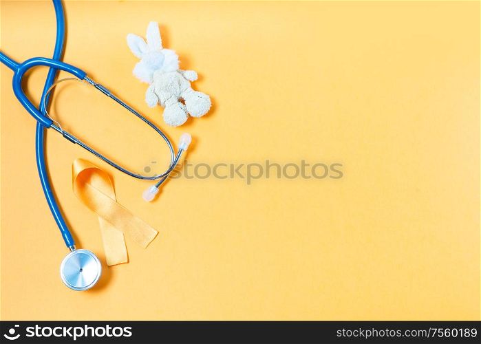 Children&rsquo;s toy rabbit with a Childhood Cancer Awareness yellow ribbon and stethoscope on yellow background with copy space, top view with copy space. Childhood Cancer Awareness concept