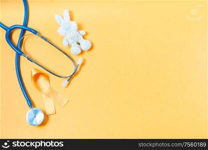 Children&rsquo;s toy rabbit with a Childhood Cancer Awareness yellow ribbon and stethoscope on yellow background with copy space, top view with copy space. Childhood Cancer Awareness concept