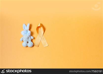 Children&rsquo;s toy rabbit with a Childhood Cancer Awareness yellow ribbon on yellow background with copy space, top view. Childhood Cancer Awareness concept