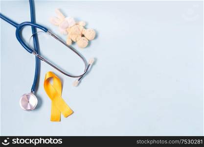 Children&rsquo;s toy rabbit with childhood cancer awareness yellow ribbon bow and stethoscope on blue background. Childhood Cancer Day February, 15. Childhood Cancer Awareness concept