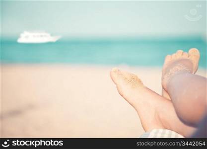 Children`s feet at the beach against sea and ship. Summer vacations concept