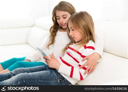 Children sister friends kid girls playing together with tablet pc on white sofa