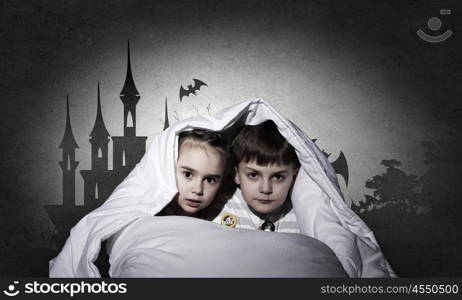 Children sitting in bed under blanket with book